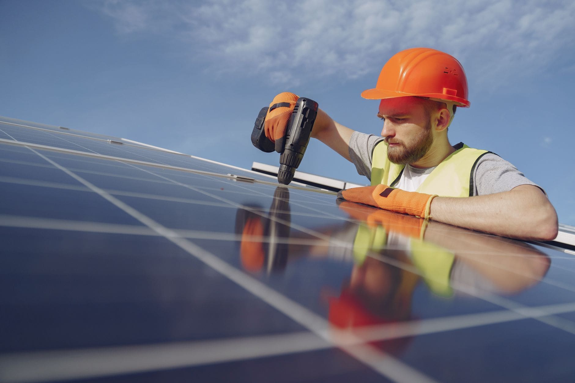 An installer in a hard hat fixing a solar panel with a drill