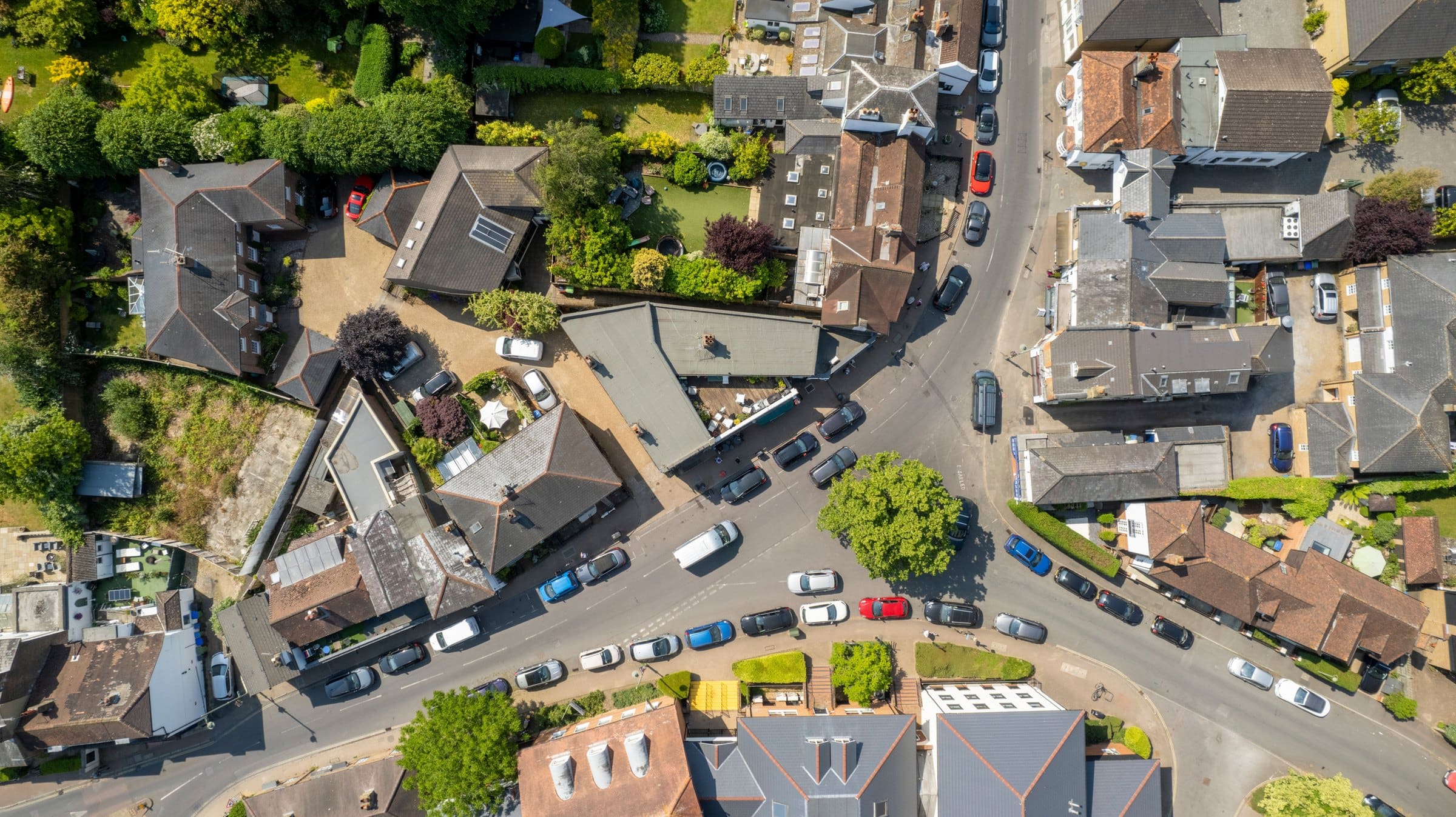 A brick house with a hipped slate roof seen straight down from the air: its chimney stack, a TV aerial, a small dormer and the trees along the garden