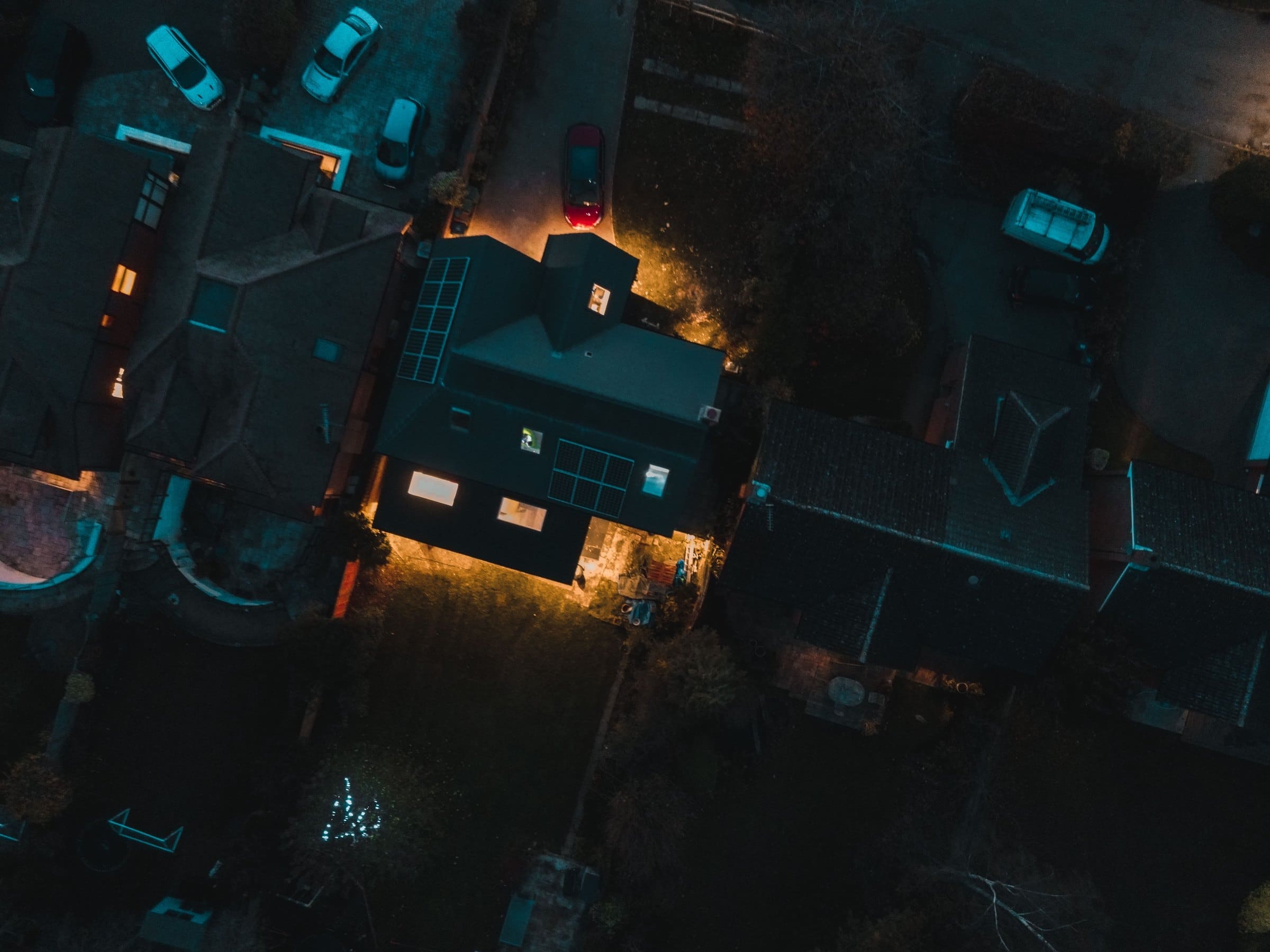 A house seen from above at night, its windows lit and solar panels on its roof