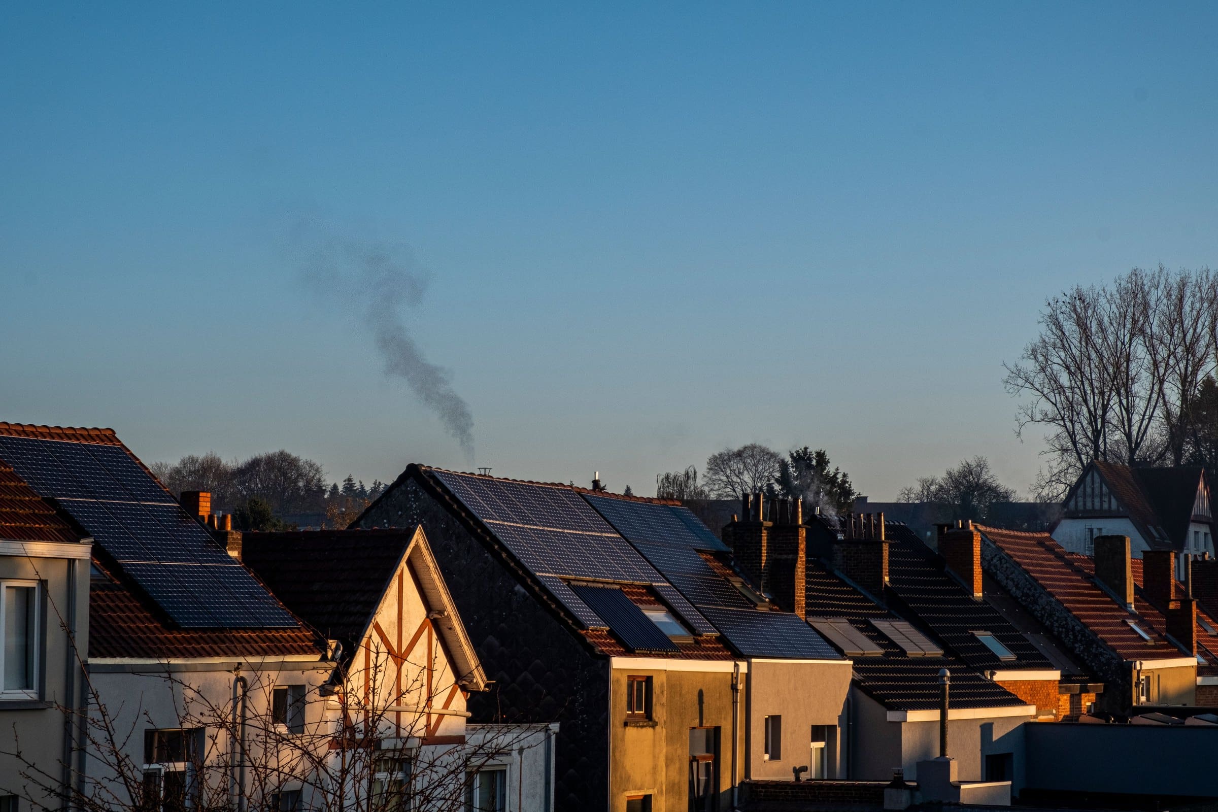Terraced rooftops carrying solar panels at first light, chimney smoke rising into a clear sky