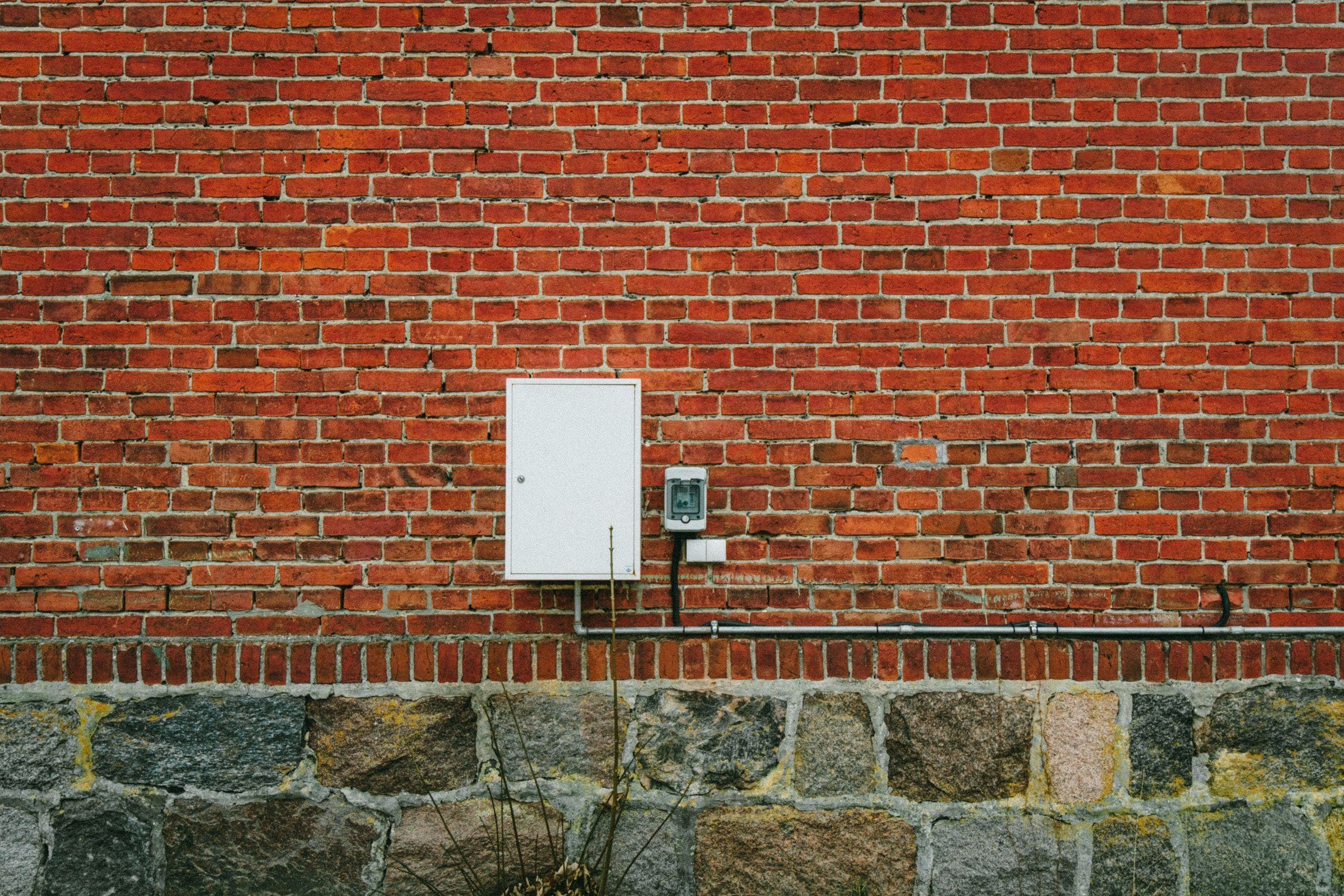 A white meter cabinet and an isolator switch on a red brick wall