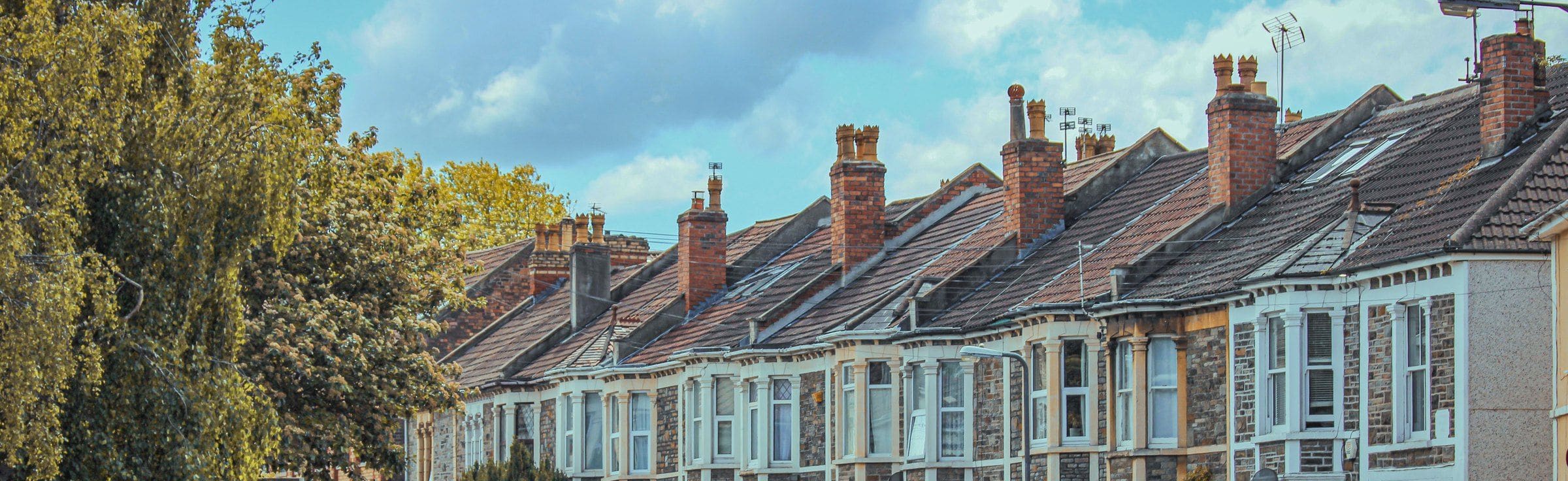 The rooflines and chimneys of a Victorian terrace under a cloudy sky
