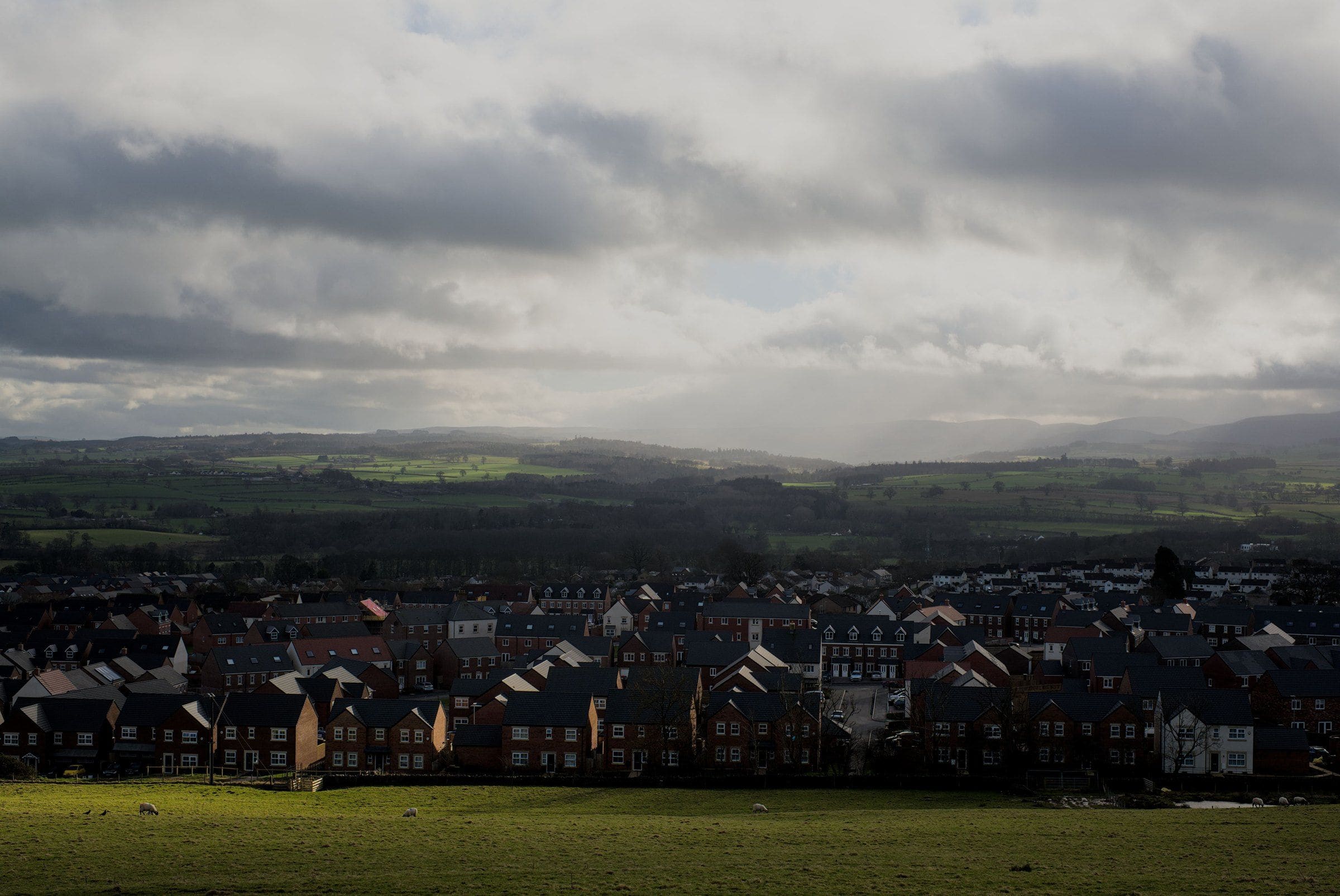 A town in a valley under a heavy evening sky, hills beyond