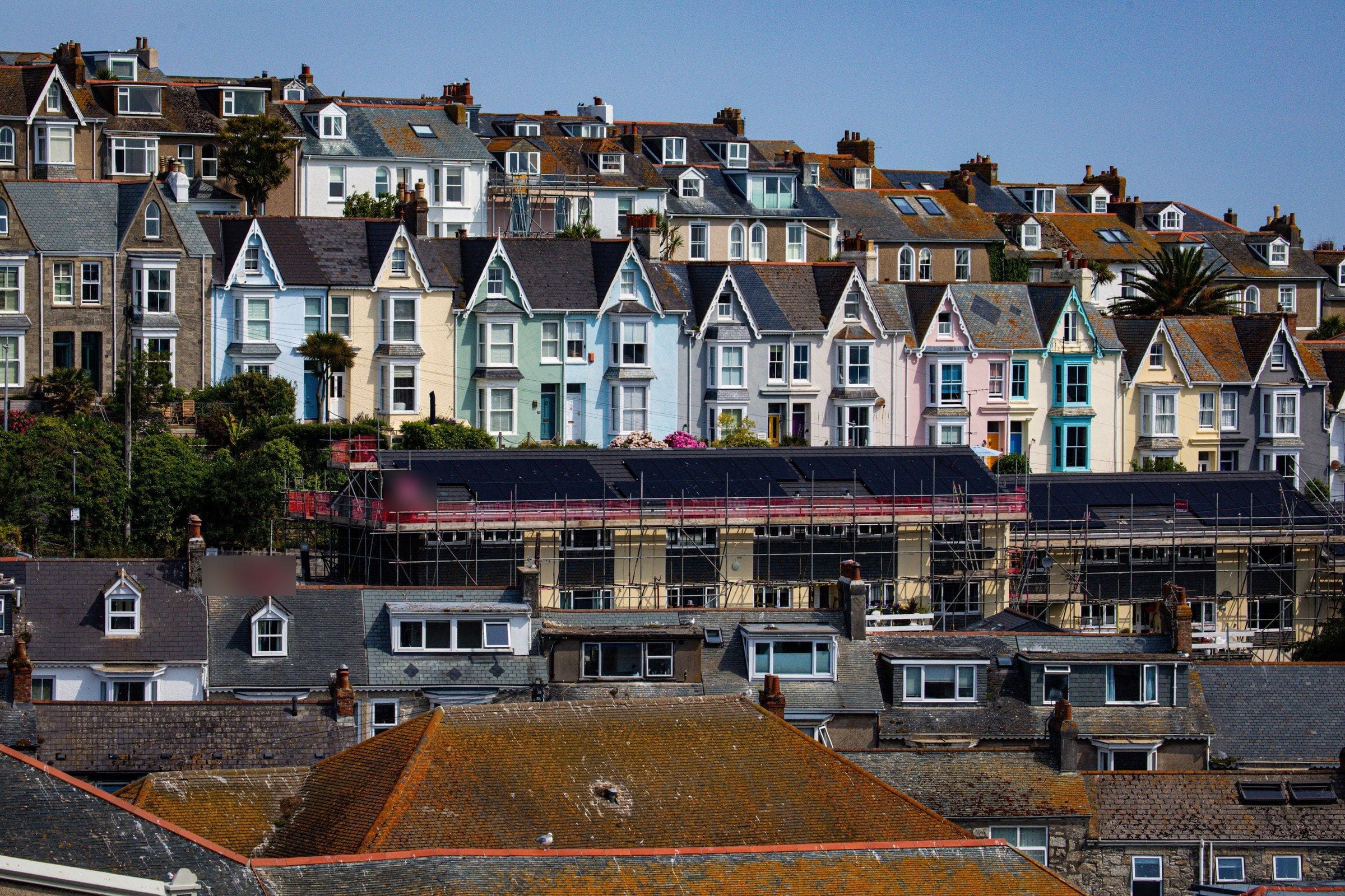 Terraced houses stepping up a hillside, one row under scaffolding with solar panels on its roof